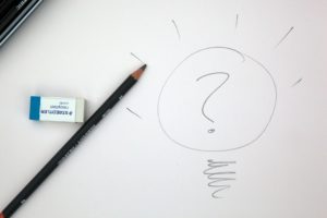 Fragezeichen in Glühbirne auf ein Blatt Papier gezeichnet. Daneben liegen Bleistift und Radiergummi.