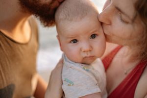 Eltern halten ihr Baby im Arm und küssen es auf den Kopf